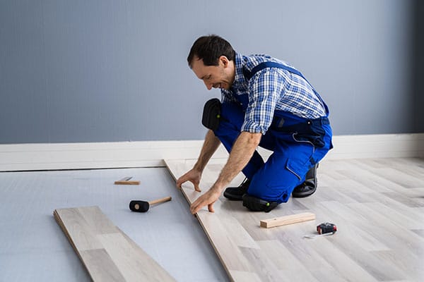 Worker installing wooden laminate flooring while kneeling on the floor in a modern room.