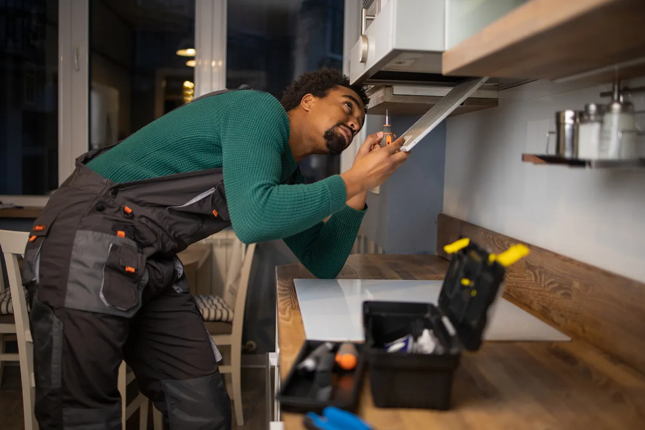 Professional technician installing modular kitchen cabinet with tools during home interior setup.
