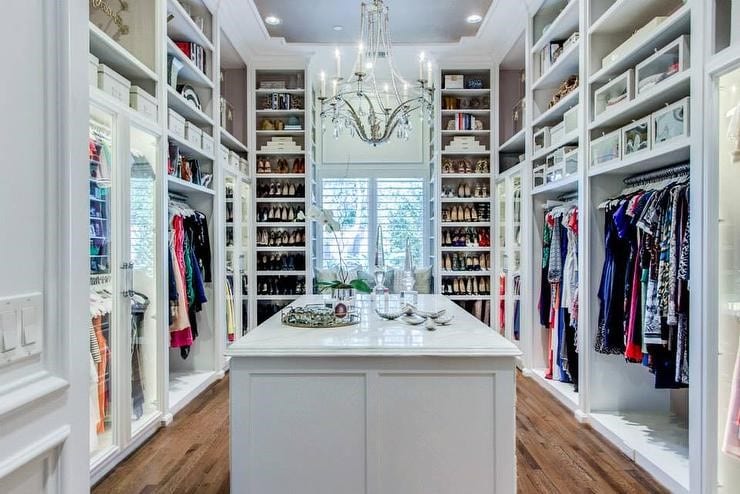 Luxurious walk-in closet with white custom shelving, a center island, hardwood floors, and a crystal chandelier.