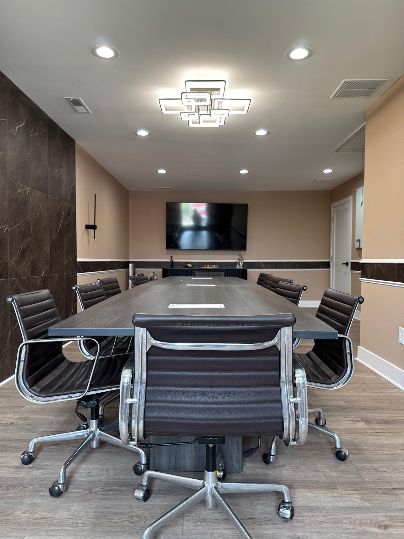 Modern conference room with large table, dark brown leather chairs, and wall-mounted TV