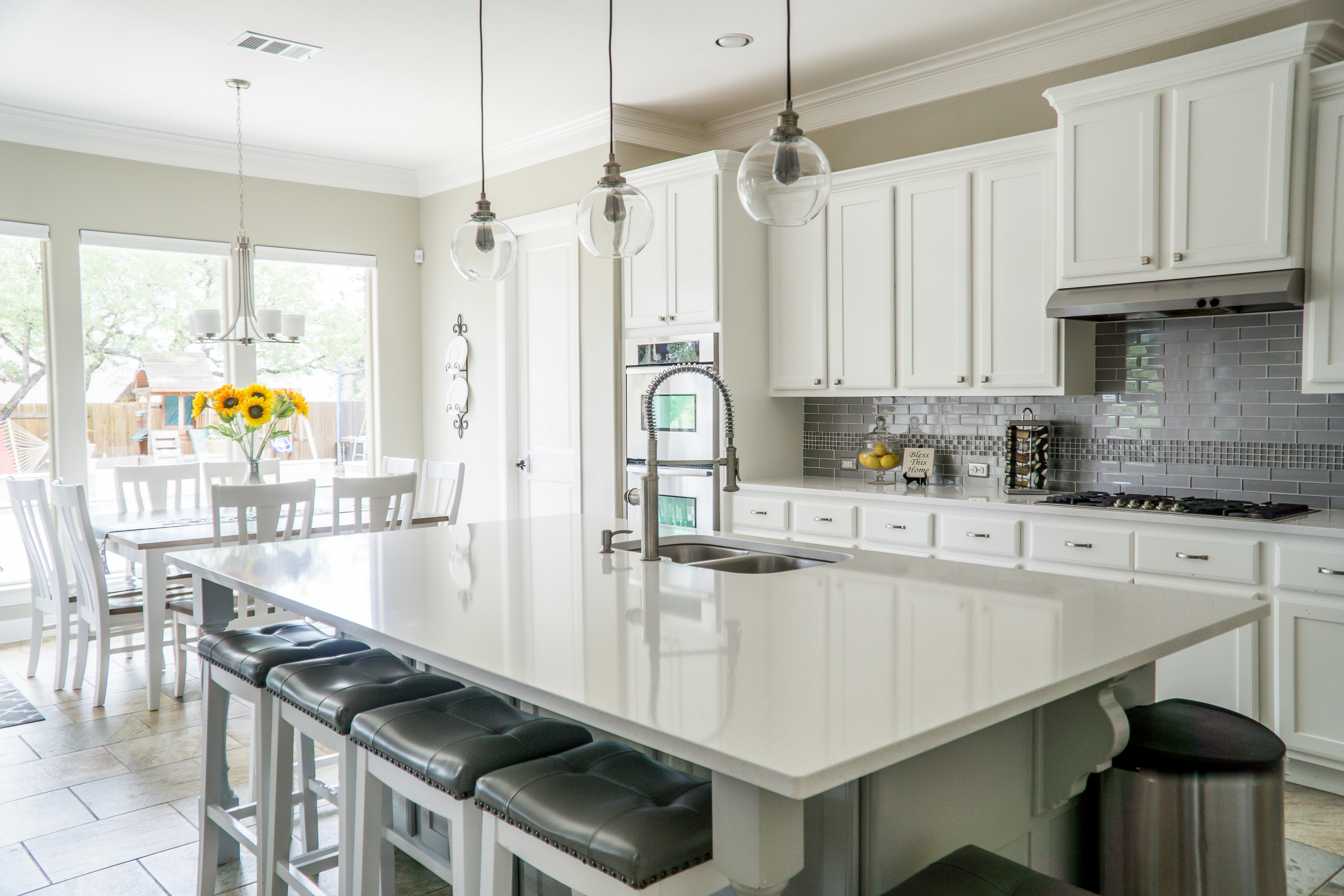 White kitchen with large island, pendant lights, and stainless steel appliances