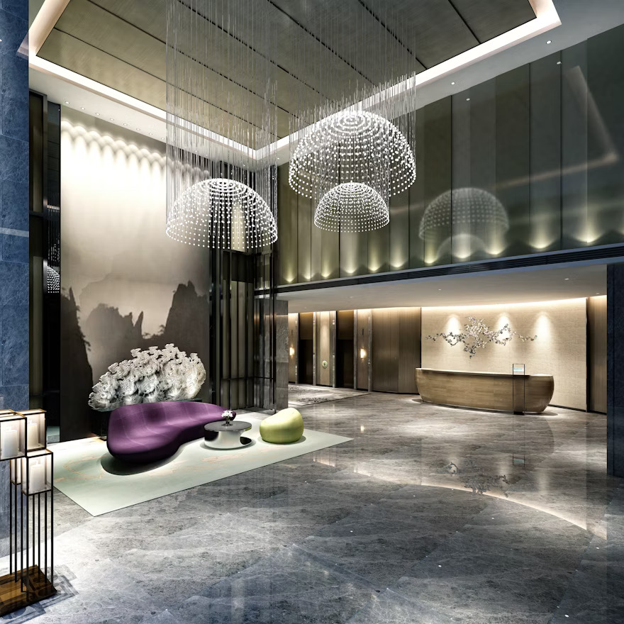 Modern hotel lobby with marble floors, elegant chandeliers, and a curved reception desk.